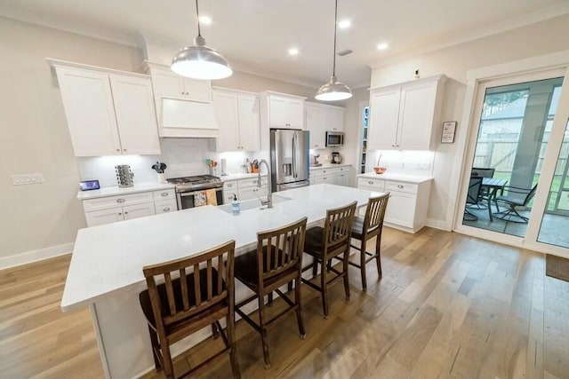 kitchen featuring stainless steel appliances, light countertops, a kitchen island with sink, white cabinetry, and extractor fan