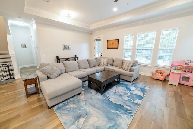 living room featuring light wood-style flooring, a tray ceiling, baseboards, and ornamental molding