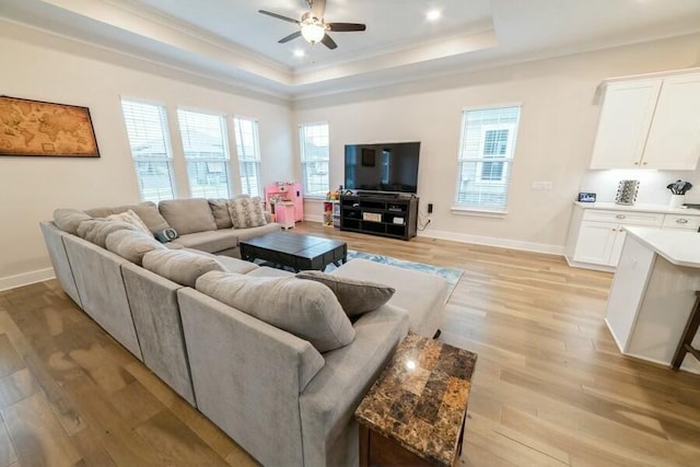 living area featuring baseboards, ceiling fan, a tray ceiling, crown molding, and light wood-type flooring