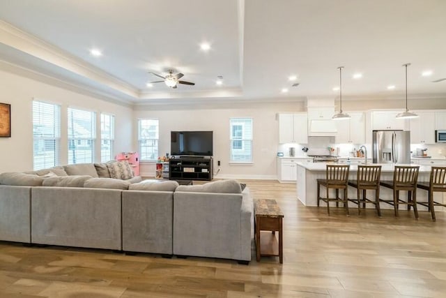 living room with light wood finished floors, ornamental molding, a raised ceiling, and a ceiling fan