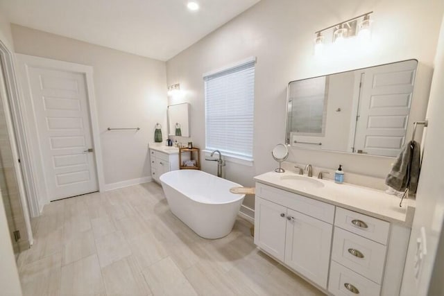 bathroom featuring a freestanding tub, two vanities, a sink, and baseboards