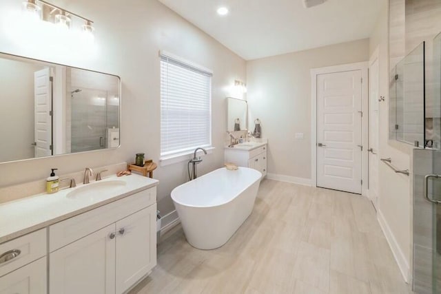 bathroom with a stall shower, two vanities, a freestanding tub, and a sink