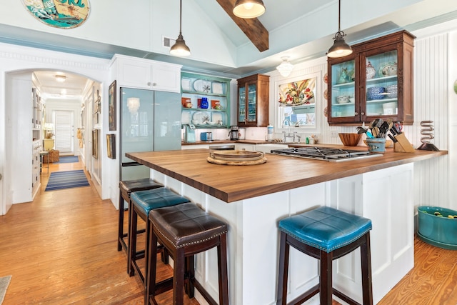 kitchen with arched walkways, stainless steel gas cooktop, butcher block counters, light wood-type flooring, and glass insert cabinets