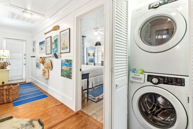 clothes washing area featuring laundry area, wood finished floors, visible vents, stacked washing maching and dryer, and crown molding