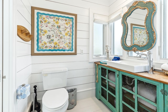 half bathroom featuring wooden walls, a healthy amount of sunlight, vanity, and toilet