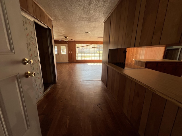 corridor with wooden walls, a textured ceiling, and wood finished floors