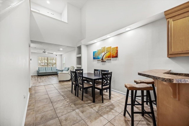 dining area with light tile patterned floors, ceiling fan, a high ceiling, and baseboards