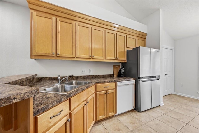 kitchen featuring a sink, vaulted ceiling, freestanding refrigerator, dishwasher, and dark countertops