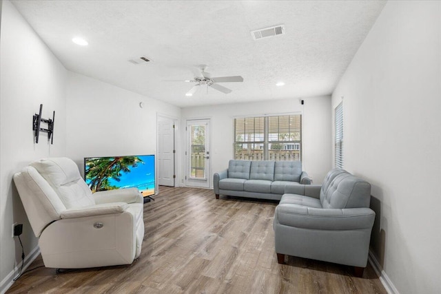 living area featuring a textured ceiling, wood finished floors, a ceiling fan, visible vents, and baseboards