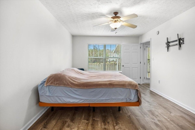 bedroom with ceiling fan, a textured ceiling, baseboards, and wood finished floors