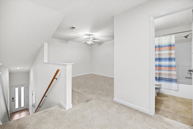 interior space with light carpet, visible vents, a textured ceiling, and an upstairs landing