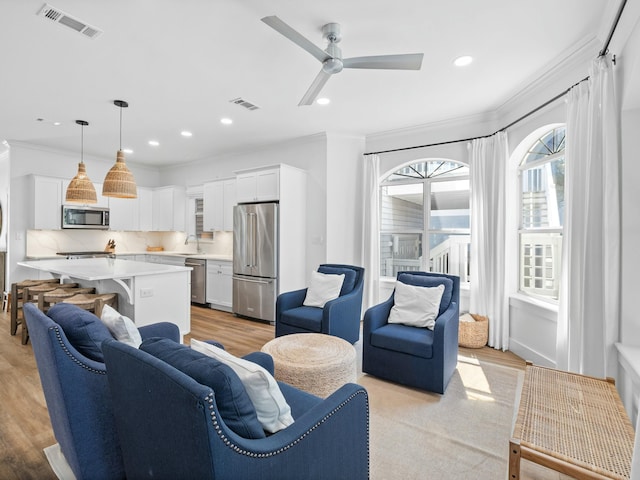 living area featuring ornamental molding, light wood-type flooring, visible vents, and a ceiling fan