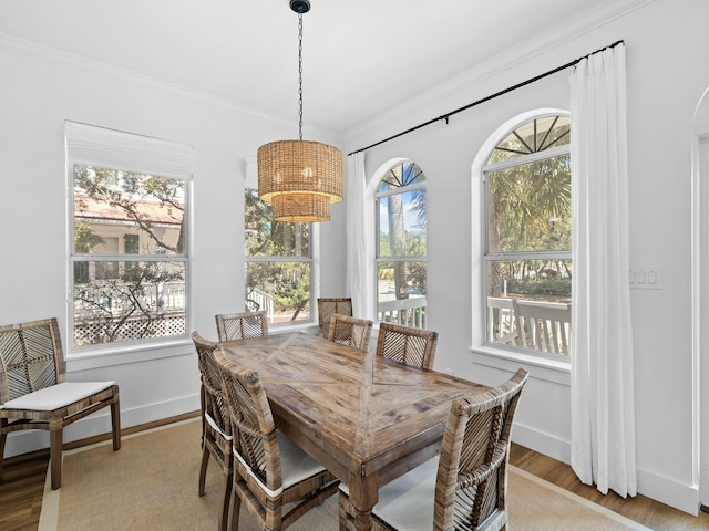 dining space featuring arched walkways, ornamental molding, light wood-type flooring, and baseboards