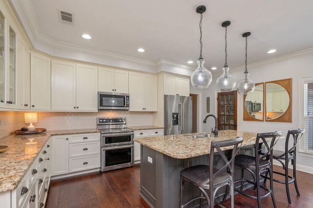 kitchen featuring an island with sink, appliances with stainless steel finishes, glass insert cabinets, and a sink