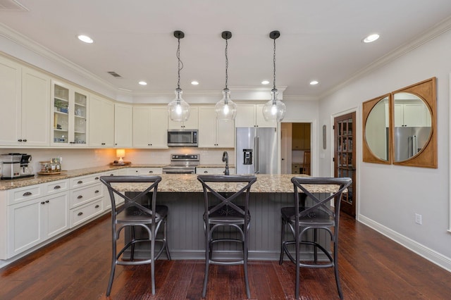 kitchen featuring glass insert cabinets, light stone counters, a kitchen island with sink, stainless steel appliances, and pendant lighting