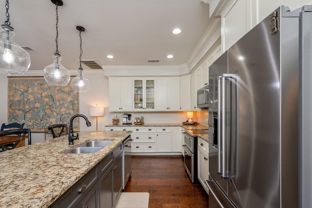 kitchen with stainless steel appliances, a sink, white cabinetry, hanging light fixtures, and glass insert cabinets