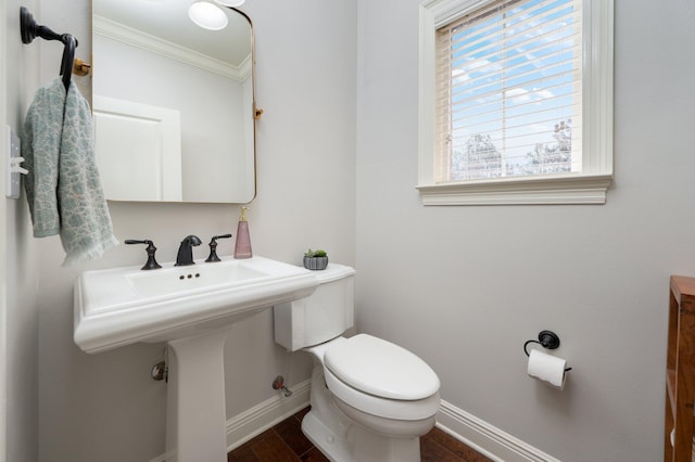 half bath with ornamental molding, wood finished floors, toilet, and baseboards