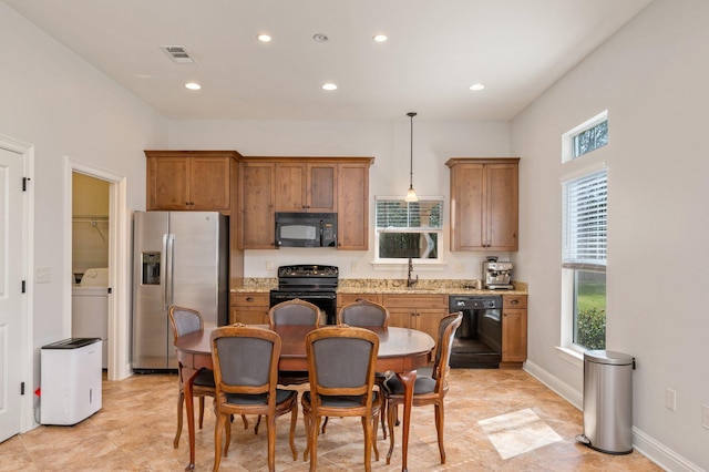 kitchen with light stone counters, pendant lighting, brown cabinets, visible vents, and black appliances