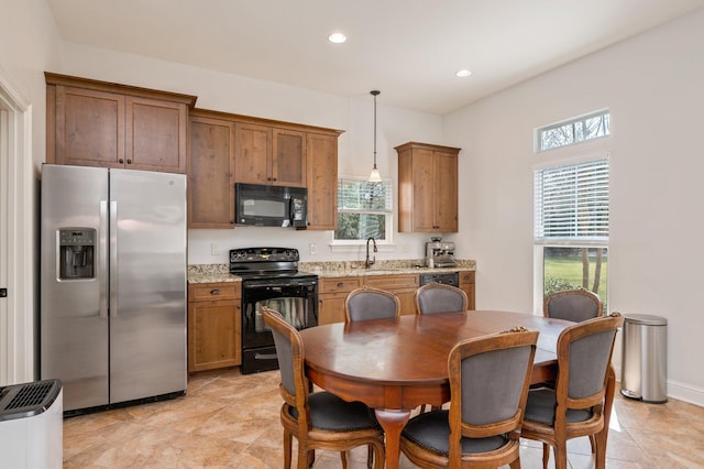 kitchen featuring brown cabinetry, light stone counters, hanging light fixtures, black appliances, and a sink