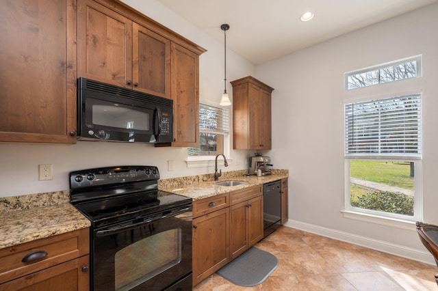 kitchen featuring brown cabinets, light stone countertops, black appliances, pendant lighting, and a sink