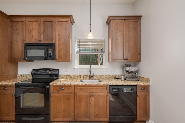 kitchen featuring hanging light fixtures, brown cabinetry, a sink, light stone countertops, and black appliances