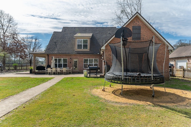 back of house featuring a trampoline, a patio area, fence, and a lawn