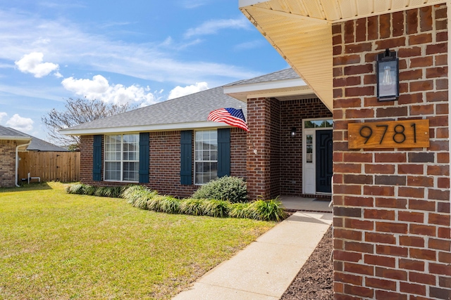 doorway to property featuring a yard, roof with shingles, fence, and brick siding