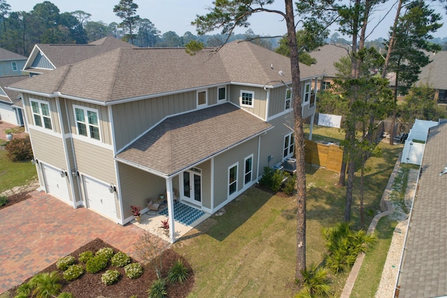 back of house with a garage, a yard, decorative driveway, and roof with shingles