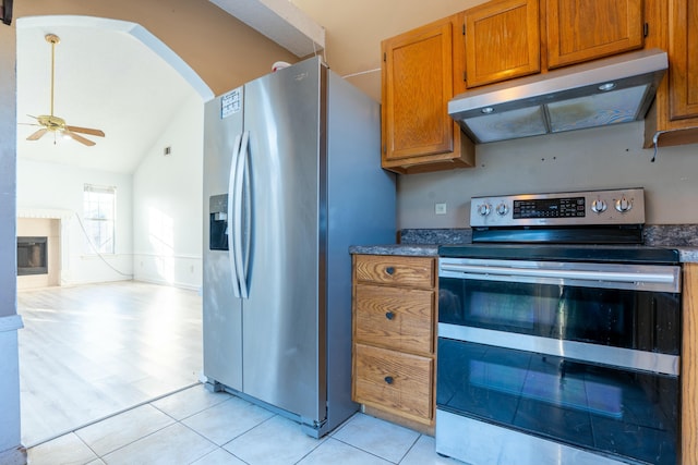 kitchen with arched walkways, extractor fan, stainless steel appliances, a fireplace, and dark countertops