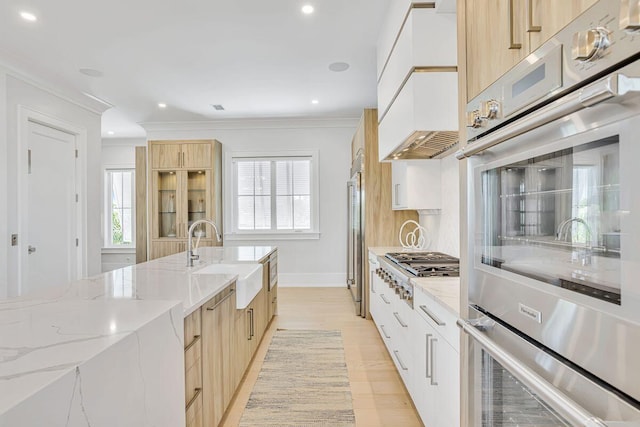 kitchen with a sink, light brown cabinetry, modern cabinets, stainless steel appliances, and crown molding