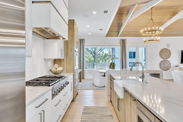 kitchen with a sink, modern cabinets, custom exhaust hood, light stone countertops, and a chandelier