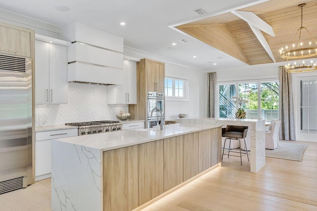 kitchen featuring stainless steel appliances, modern cabinets, decorative backsplash, a chandelier, and light stone counters