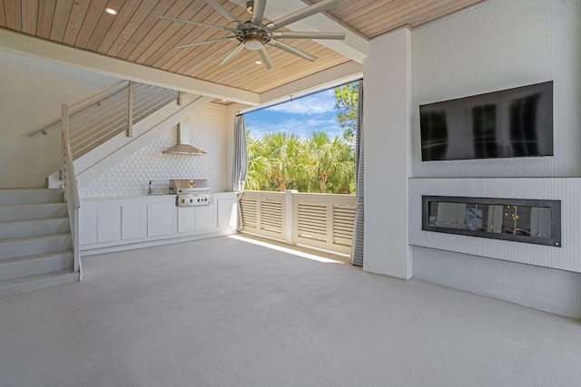 unfurnished living room featuring stairway, ceiling fan, wooden ceiling, carpet floors, and a glass covered fireplace