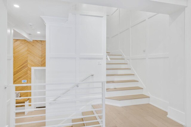 stairs with wood finished floors, recessed lighting, and wood walls