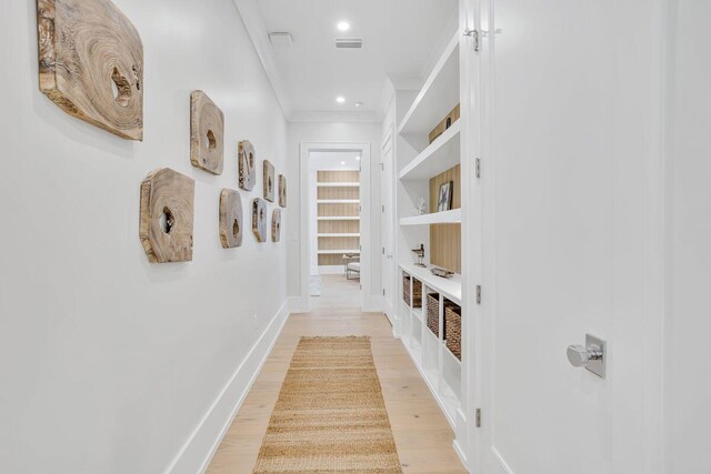 corridor featuring crown molding, built in features, light wood-type flooring, baseboards, and recessed lighting