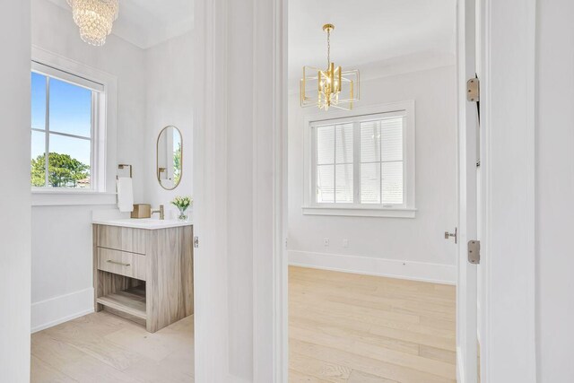 corridor with a chandelier, baseboards, and light wood finished floors