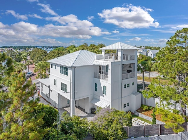 rear view of property featuring stucco siding, a standing seam roof, metal roof, fence, and a balcony