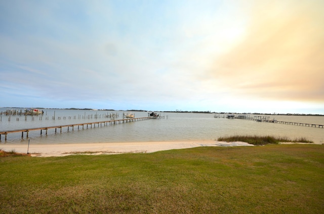 view of dock with a lawn and a water view