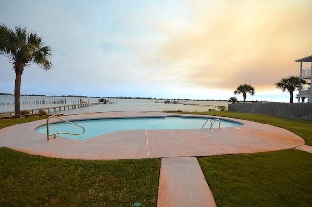 pool at dusk featuring a water view, a fenced in pool, fence, and a lawn