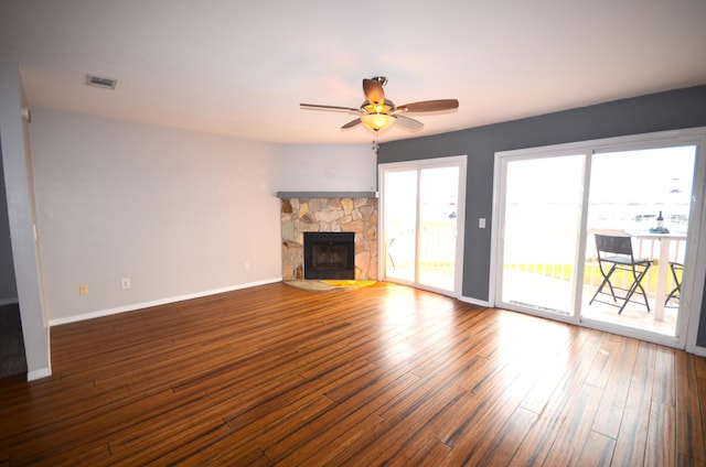 unfurnished living room featuring visible vents, a stone fireplace, baseboards, and wood finished floors