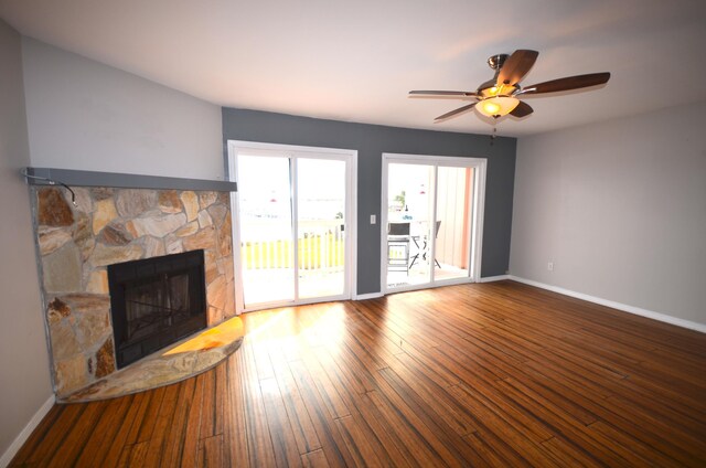 unfurnished living room featuring a stone fireplace, hardwood / wood-style floors, a ceiling fan, and baseboards