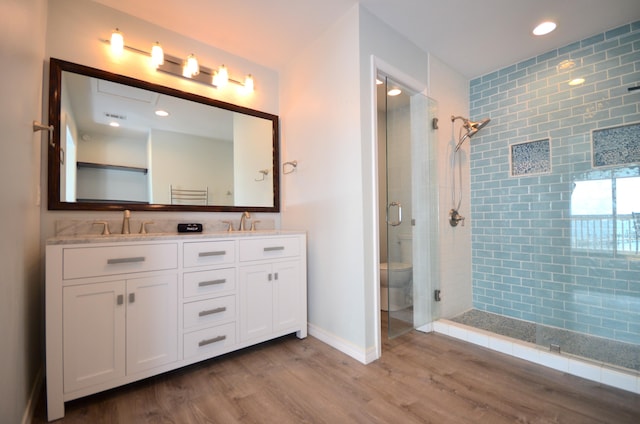 full bathroom featuring double vanity, toilet, a stall shower, a sink, and wood finished floors