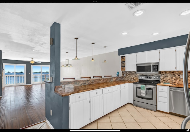 kitchen with stainless steel appliances, a water view, white cabinetry, backsplash, and ceiling fan