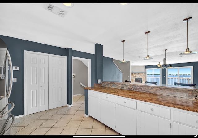 kitchen with light tile patterned floors, a fireplace, white cabinets, stainless steel refrigerator with ice dispenser, and visible vents