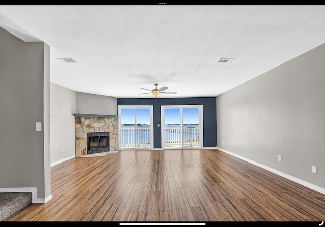 unfurnished living room with wood finished floors, visible vents, a ceiling fan, baseboards, and a fireplace
