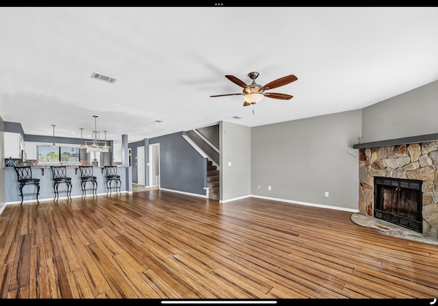 unfurnished living room featuring stairs, a stone fireplace, ceiling fan, baseboards, and visible vents