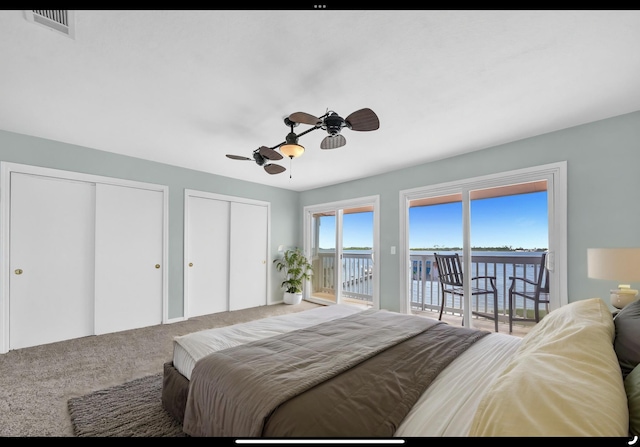 carpeted bedroom with multiple closets, a water view, access to exterior, a ceiling fan, and visible vents