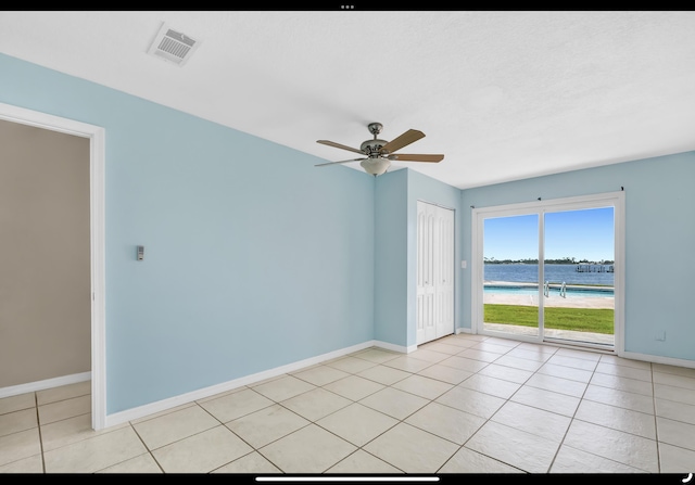 spare room featuring a water view, light tile patterned flooring, baseboards, visible vents, and a ceiling fan