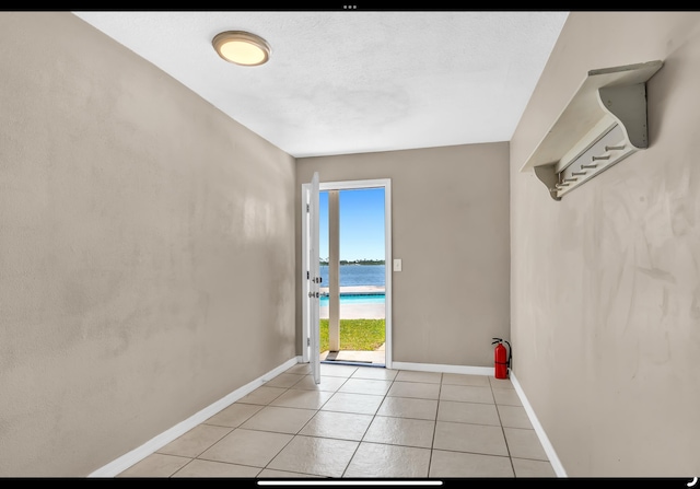 empty room featuring baseboards, a water view, and light tile patterned floors