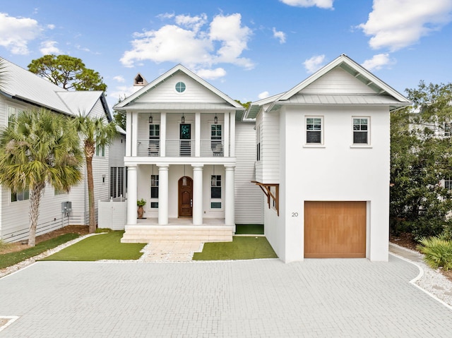 neoclassical home with metal roof, a balcony, a garage, decorative driveway, and a standing seam roof